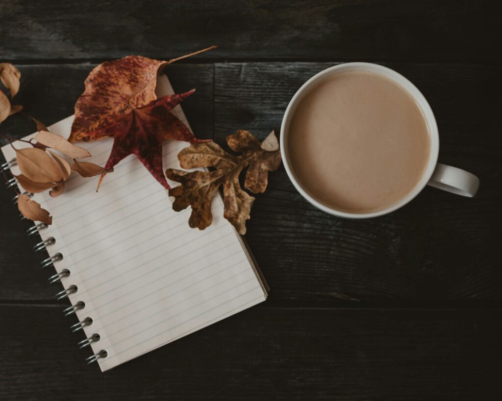Open notebook with autumn leaves and a cup of coffee on a wooden table — symbolizing fall renewal, fresh routines, and seasonal self-care.